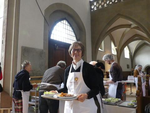 Regionalbischöfin Gisela Bornowski in Vesperkirche-Schürze trägt ein Tablett mit Essen